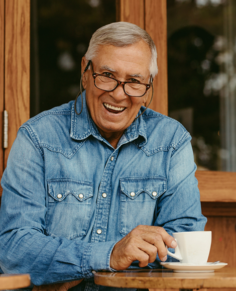 Senior man with denim jacket smiling and picking up coffee cup